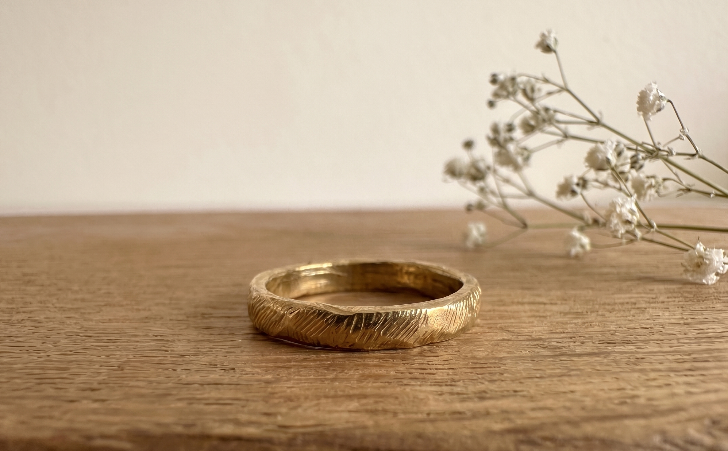 Anillo rústico de bronce hecho a mano sobre mesa de madera, con textura facetada