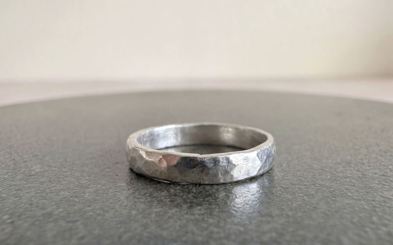 Anillo de plata martillado Ley 950 hecho a mano, vista lateral sobre superficie gris