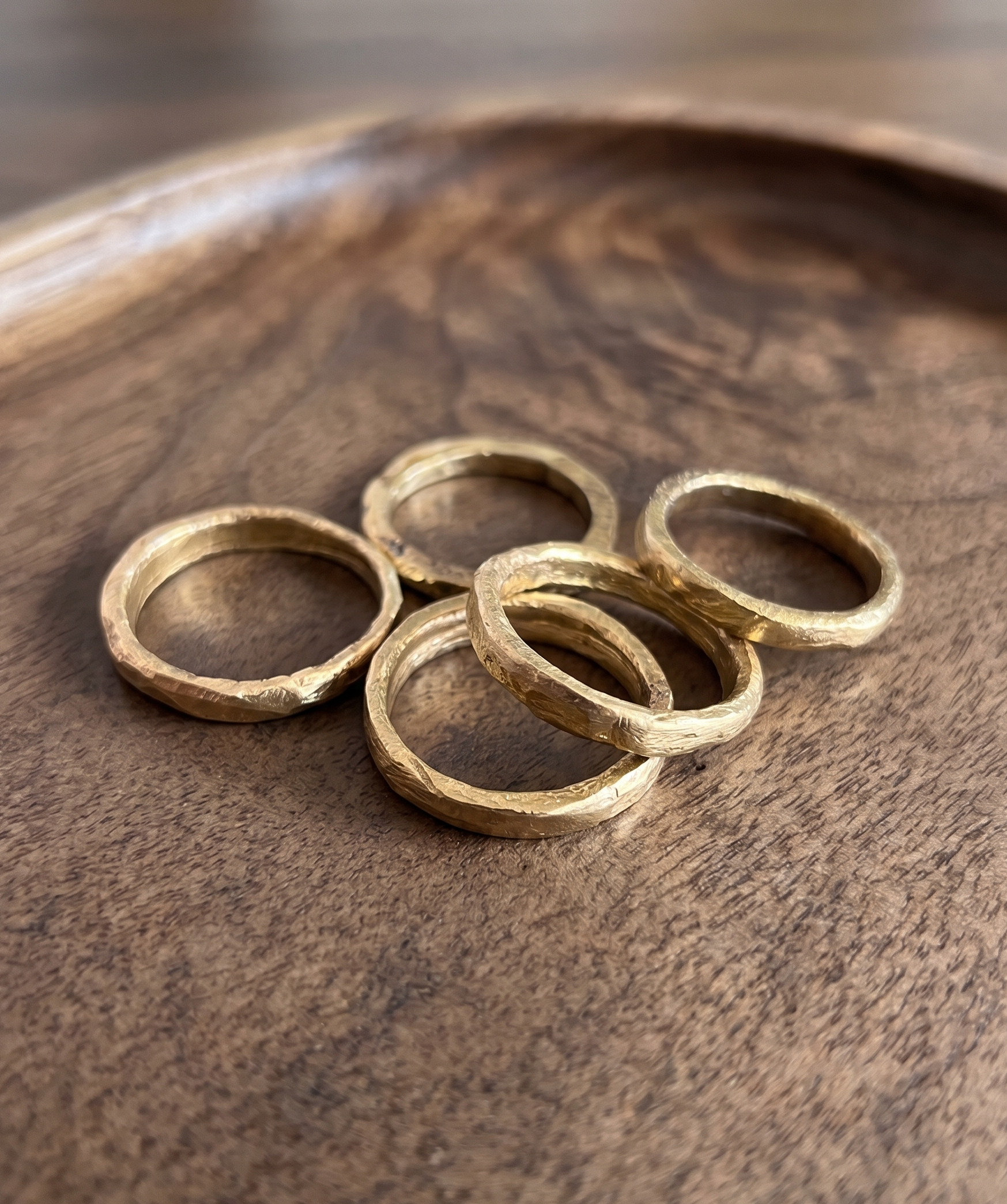 Varios anillos rústicos de bronce en un plato de madera, cada pieza con textura irrepetible