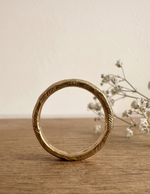 Anillo rústico de bronce de pie, mostrando su banda cerrada y textura facetada artesanal